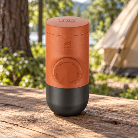 Wacaco Minipresso GR2 Portable Espresso Maker in Copper Clay on a wooden table at a woodland campsite