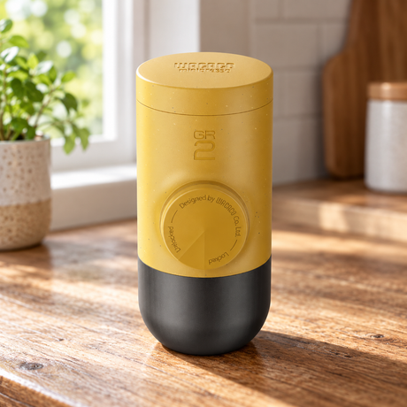 Wacaco Minipresso GR2 Portable Espresso Maker in Golden Ochre on a wooden kitchen table beside a window