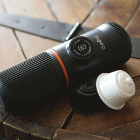 Wacaco Nanopresso fitted with DG Kit beside coffee capsules on a wooden table
