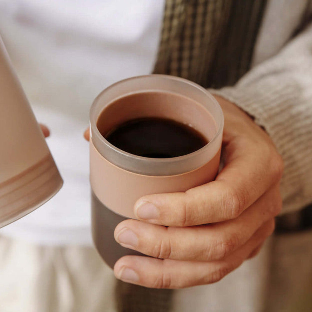 Holding a Clay Pink Wacaco Prestina and its cup of freshly brewed coffee
